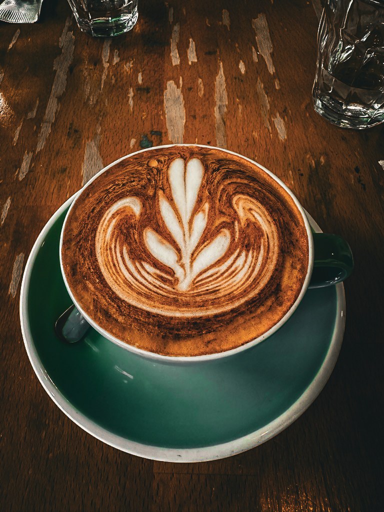 Leaf shaped latte art in a deep green cup on a wooden café table